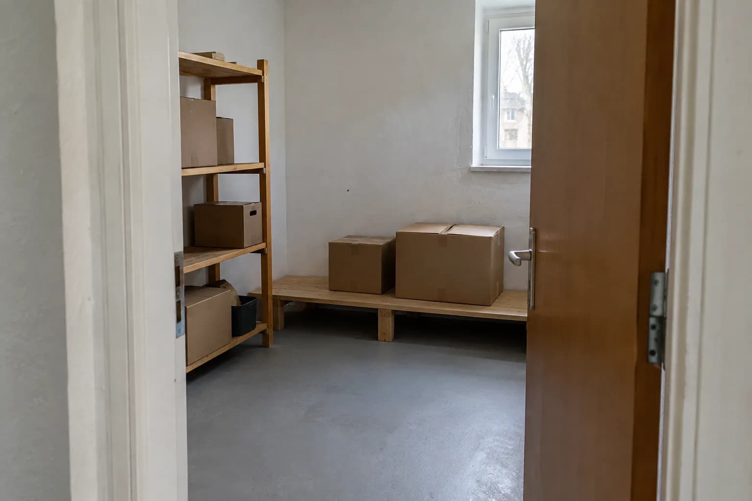 Separater Abstellraum mit Kartons im Holzregal und freiem Weg durch die Tür